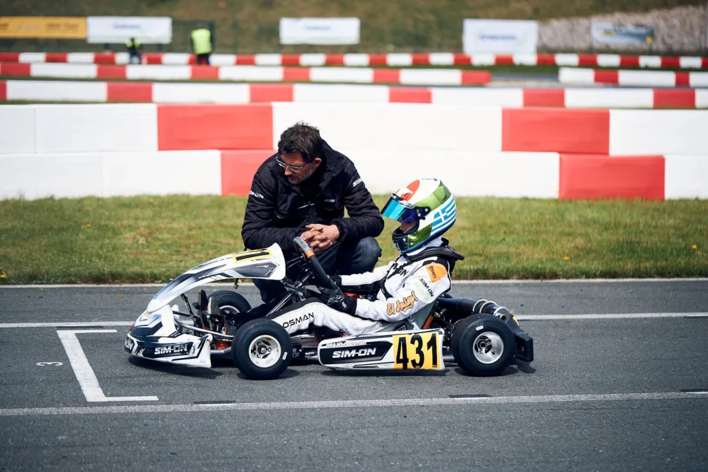 Mann kniet neben stehenden Kart auf Startlinie und spricht mit Fahrer